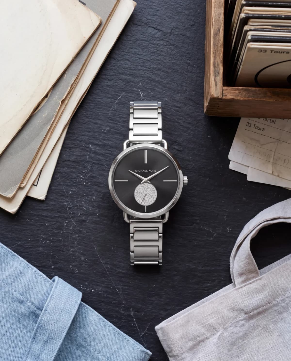 Montre Michael Kors Portia MK3638 à bracelet acier posée sur un comptoir en ardoise, petit disquaire parisien, lumière matinale